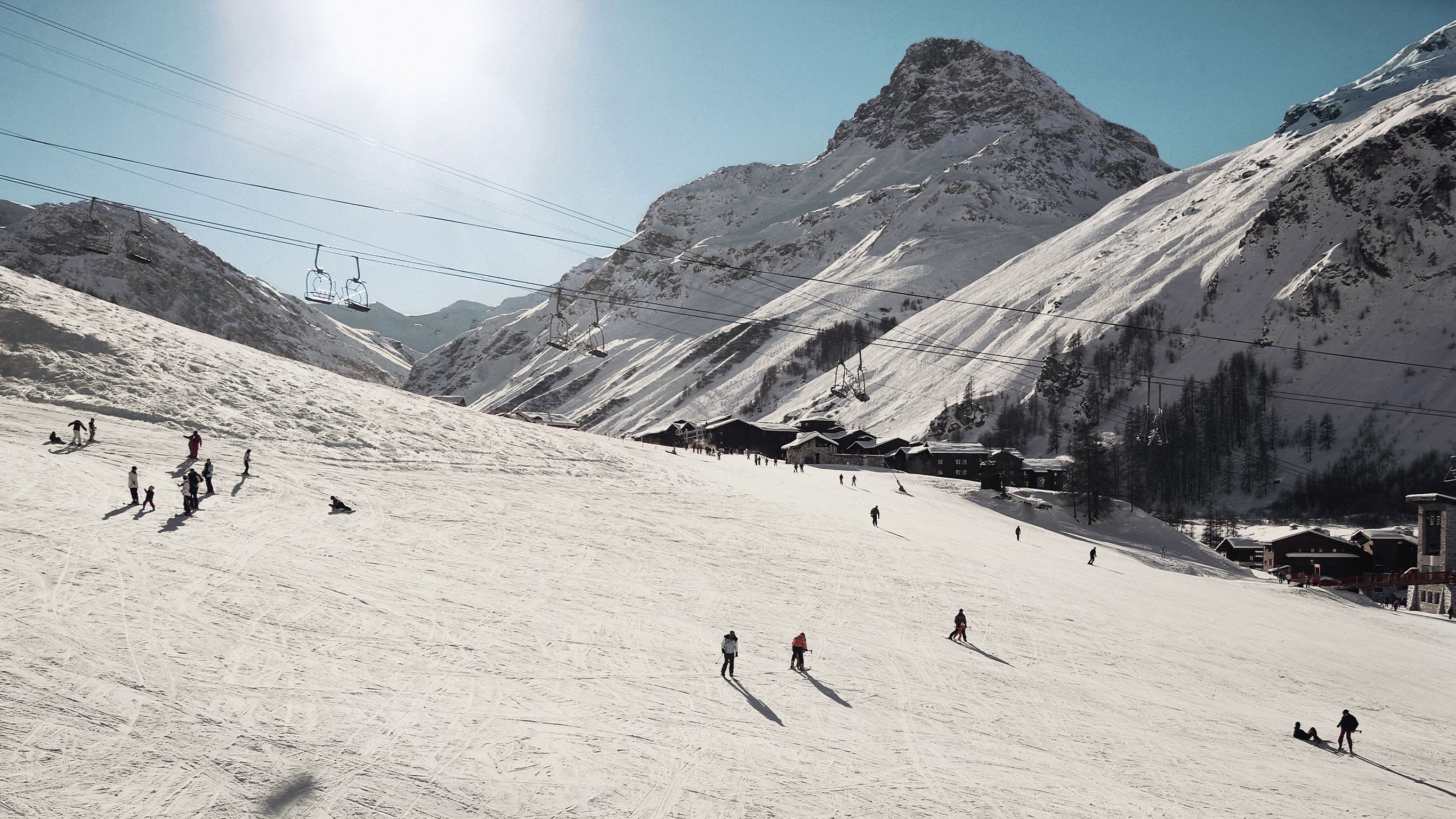 Skiers on a snowy mountain slope with chairlifts and alpine lodges in the background in Courchevel.
